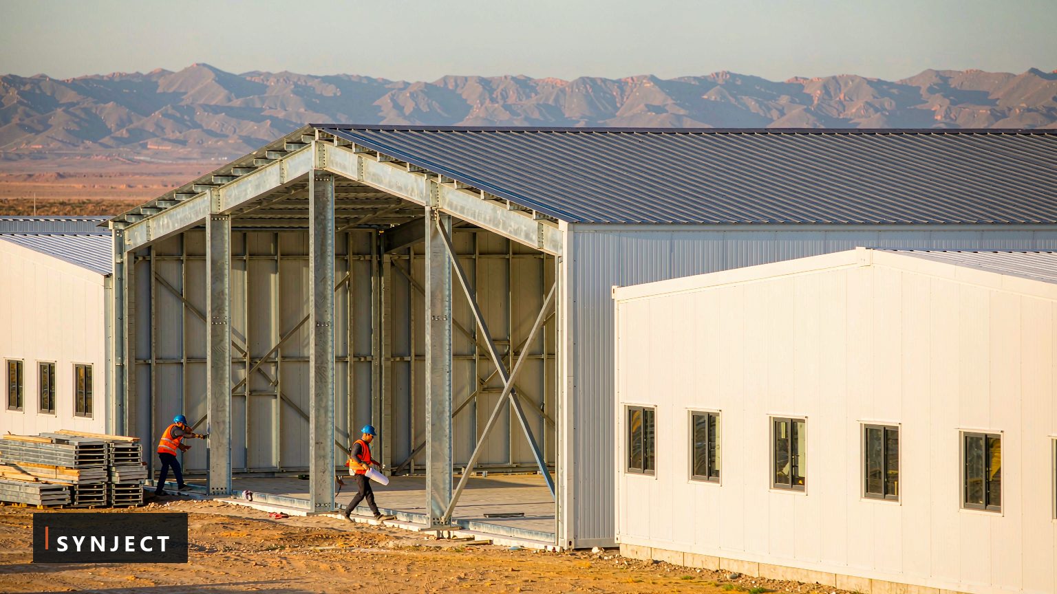 SynJect prefabricated steel training base buildings under assembly on an arid site