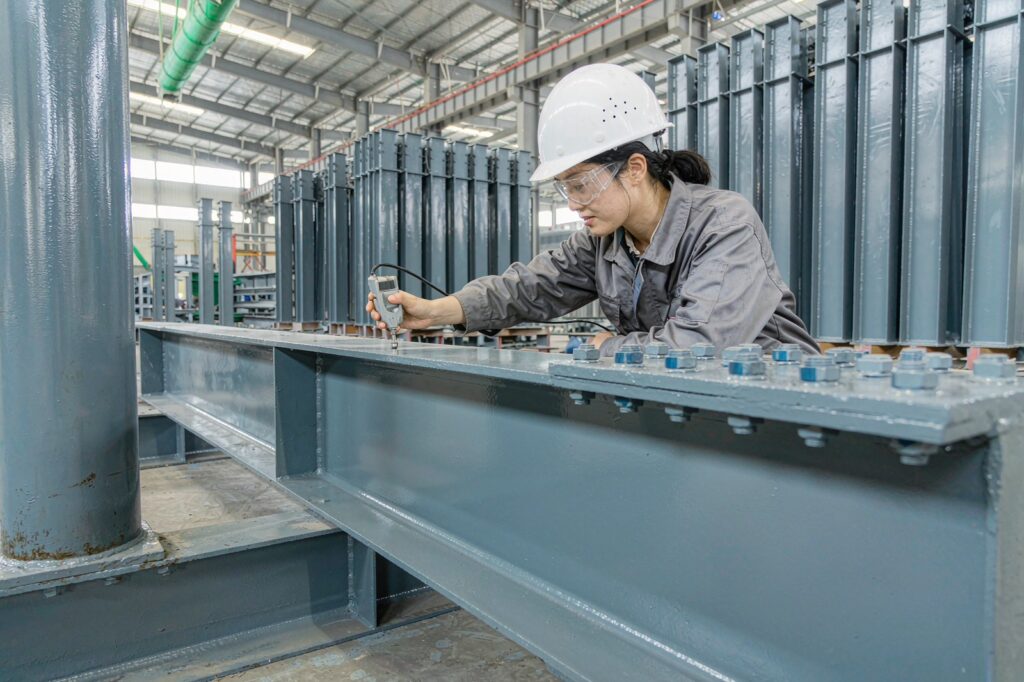 Coating inspector measuring dry film thickness on a primed steel column in a fabrication shop