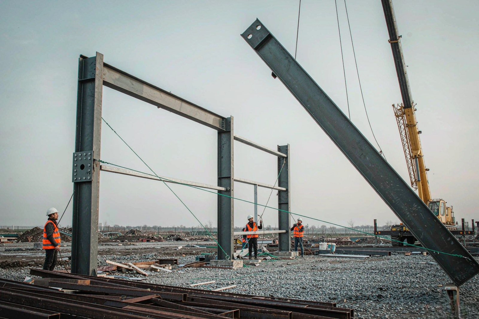 Steel structure construction site with a crawler crane lifting a welded portal frame rafter into position