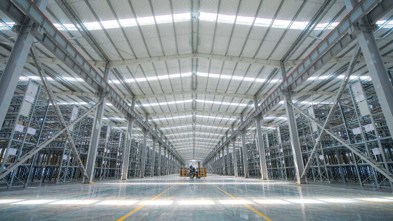 Column-free 30 m clear-span steel warehouse interior with high-bay racking, skylights and painted aisle lines